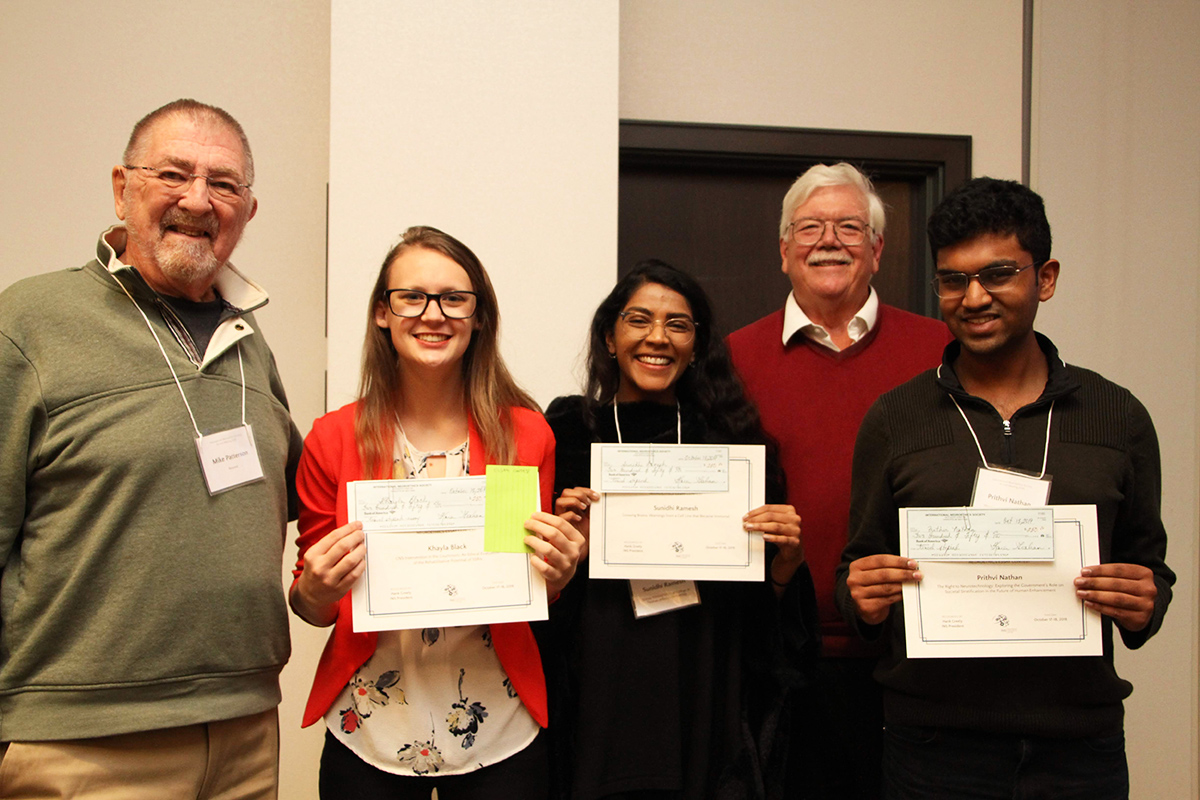 Photo of Michael Patterson presenting essay contest winners Khayla Black, Sunidhi Ramesh and Prithvi Nathan, with Hank Greely standing behind the winners